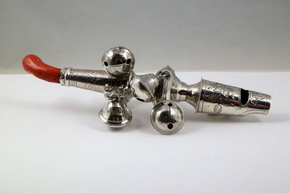 A George III sterling silver baby rattle featuring attached suspended bells, an engraved whistle, and a curved red coral handle.