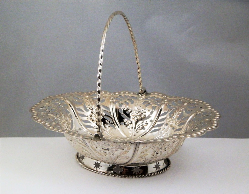 A Georgian sterling silver bonbon basket featuring hand-pierced floral lattice decoration, a twisted overhead swing handle, and a scalloped rim.