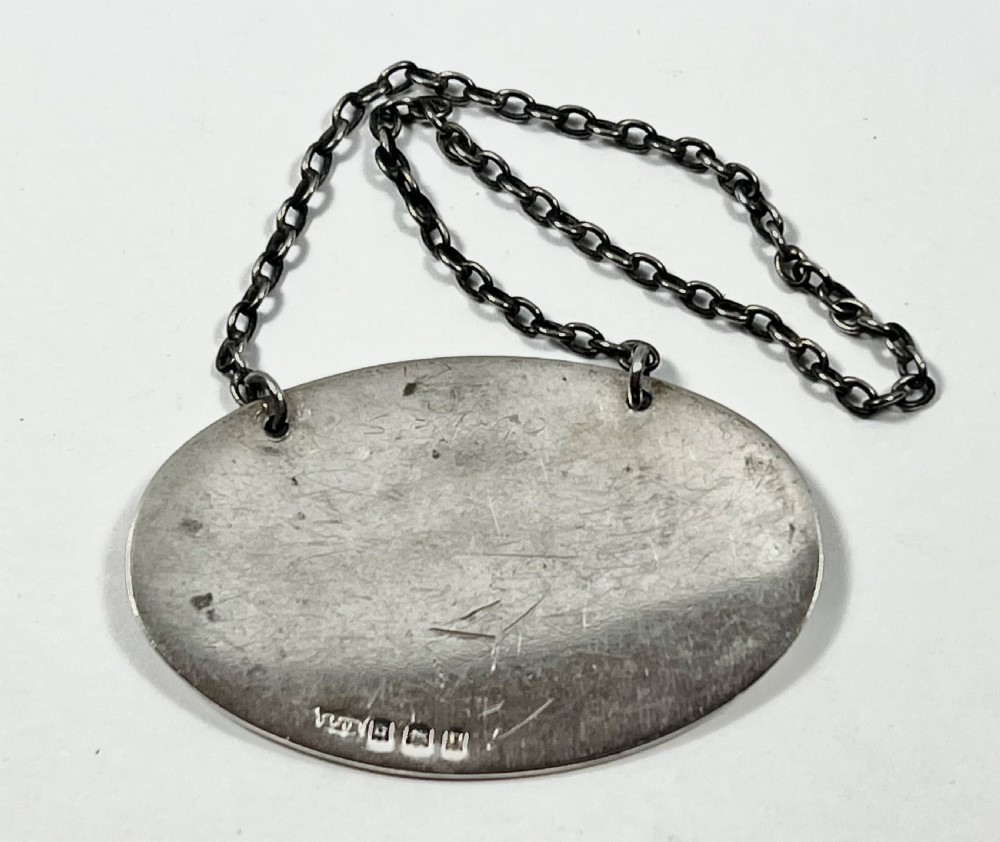 An oval sterling silver decanter label engraved with the word SHERRY and an engine-turned border pattern, suspended from a silver chain. View III