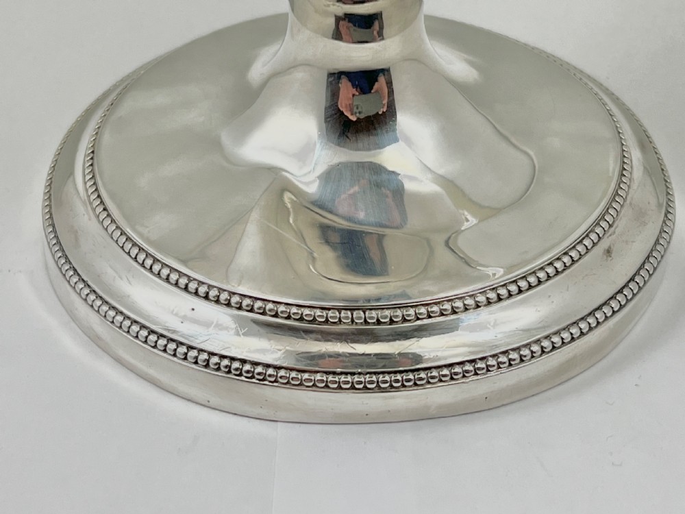 An urn-shaped sterling silver ewer with beaded border trim, a pinecone finial, and a high arched wooden handle. View II