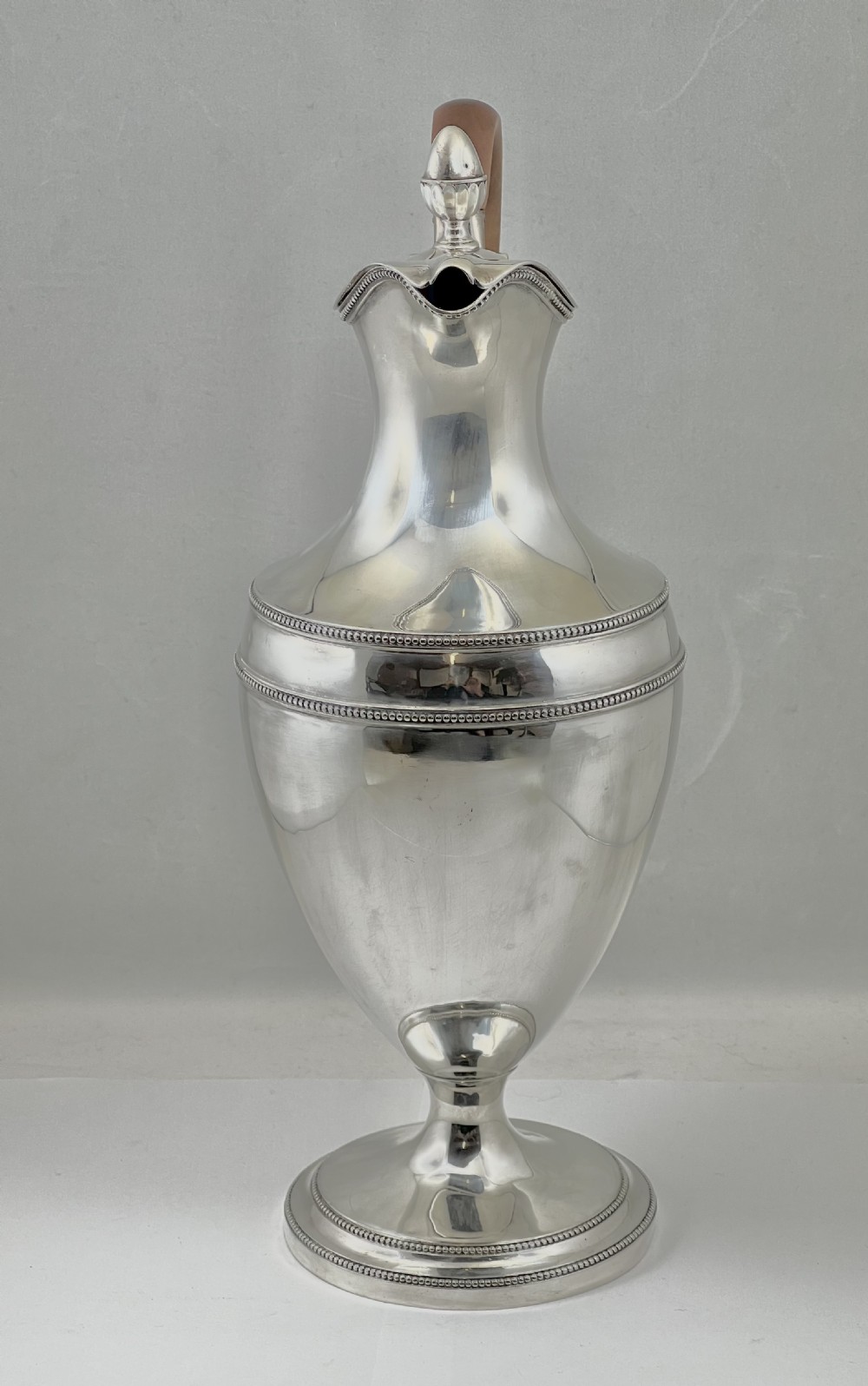 An urn-shaped sterling silver ewer with beaded border trim, a pinecone finial, and a high arched wooden handle. View VII