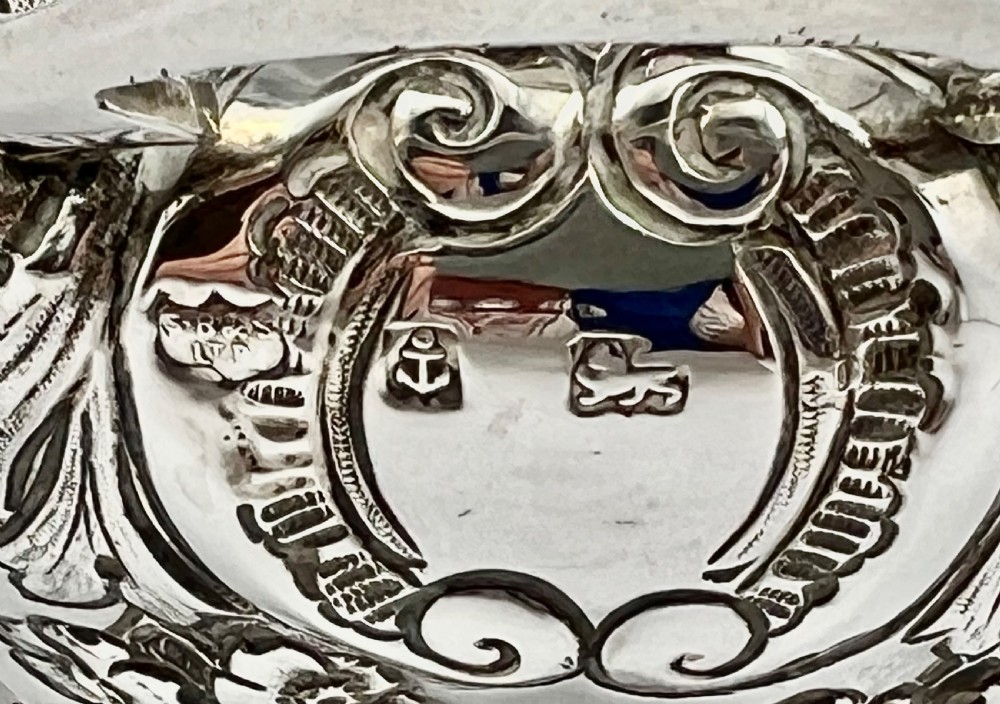 A sterling silver tea caddy featuring twin side handles, relief repousse floral scrollwork, and a domed lid topped with a dark fluted finial. View V