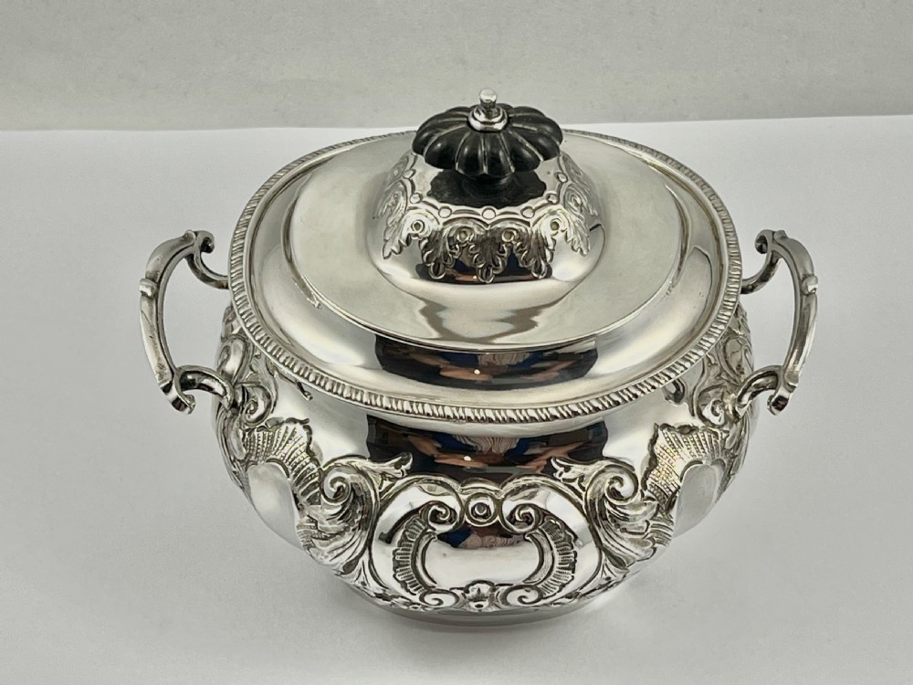A sterling silver tea caddy featuring twin side handles, relief repousse floral scrollwork, and a domed lid topped with a dark fluted finial. View VIII