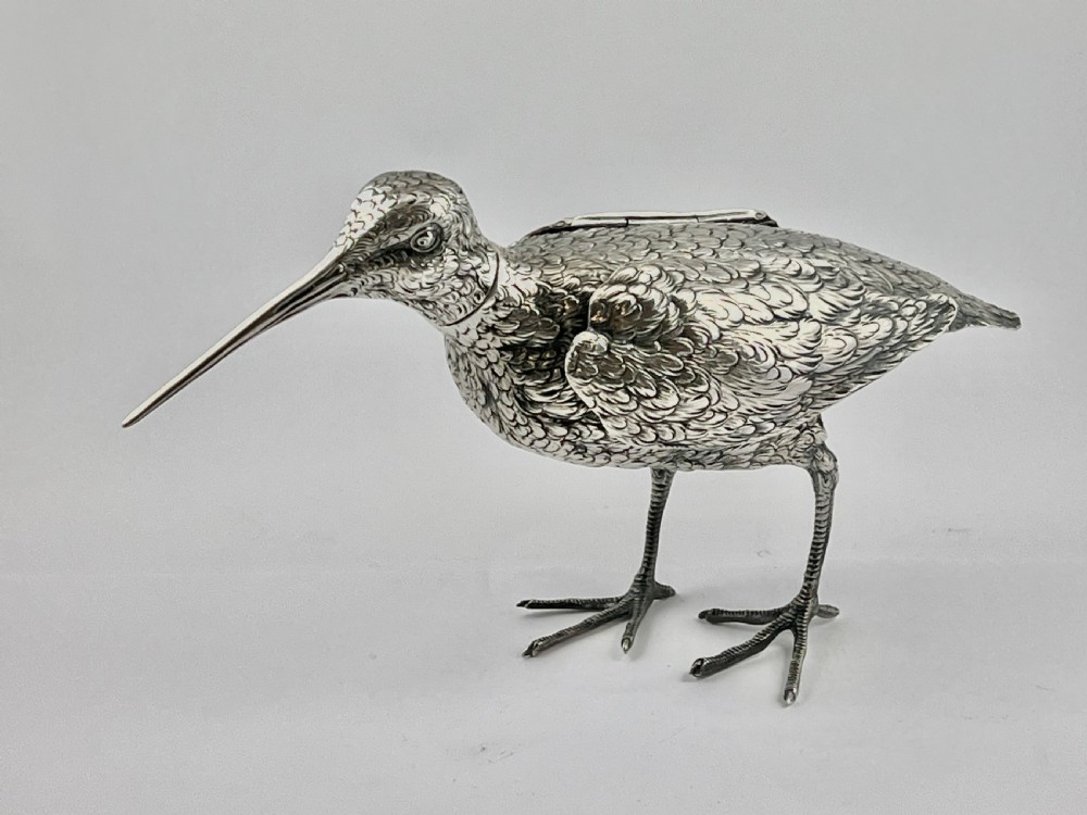 An antique silver woodcock figure depicted standing with realistic chased feather detailing and a long slender beak.