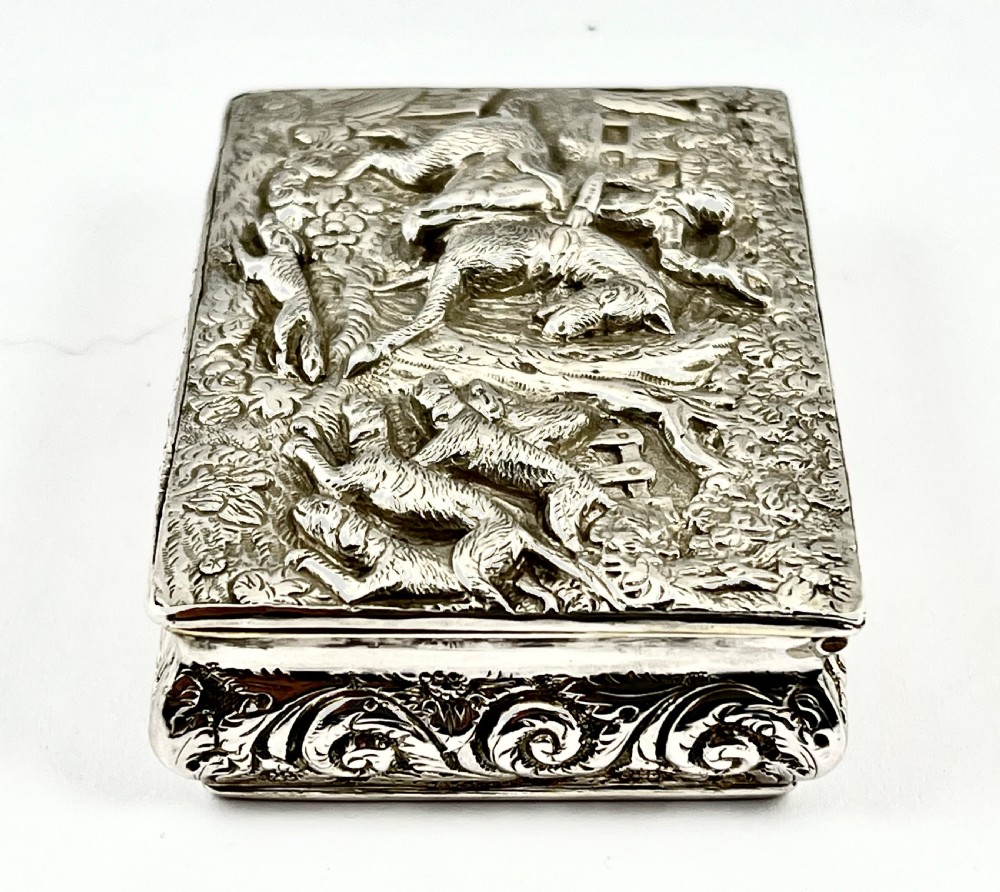 Rectangular sterling silver snuff box featuring a relief-carved hunting scene with a rider on horseback surrounded by hounds in a woodland setting. View II