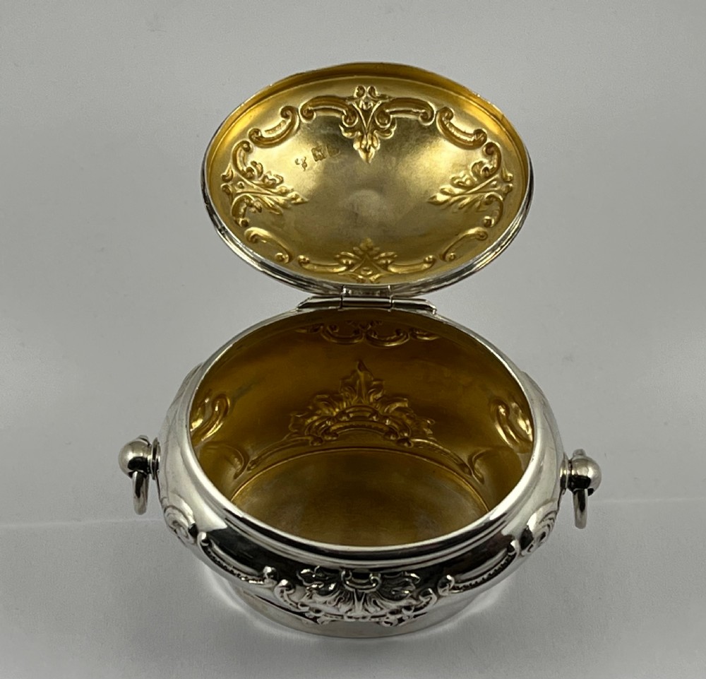 An Edwardian sterling silver tea caddy featuring repousse scrollwork motifs, twin drop handles, and a fitted lid with a finial. View VI