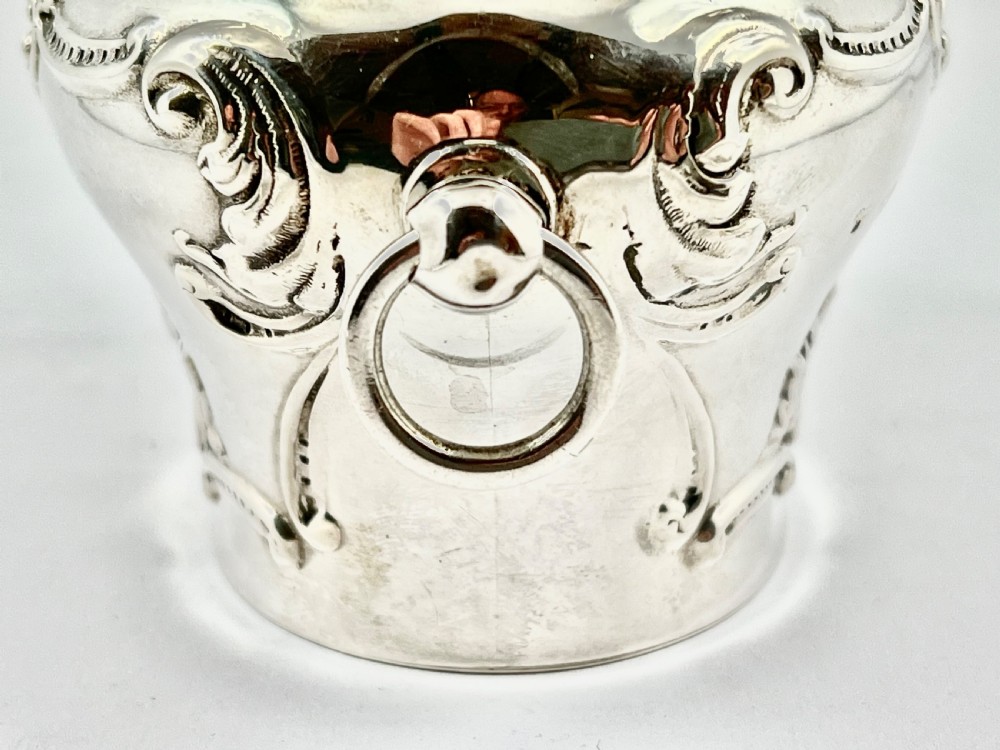 An Edwardian sterling silver tea caddy featuring repousse scrollwork motifs, twin drop handles, and a fitted lid with a finial. View IX