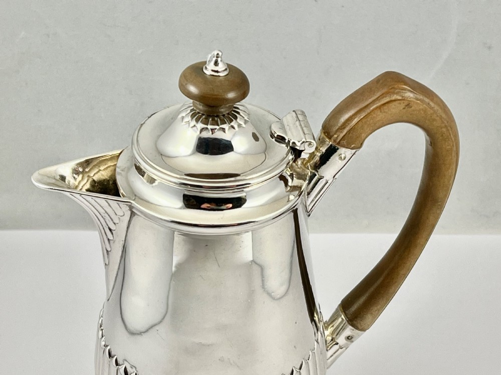 Victorian sterling silver hot water pot featuring a fluted lower body, hinged lid, and carved wooden handle. View V