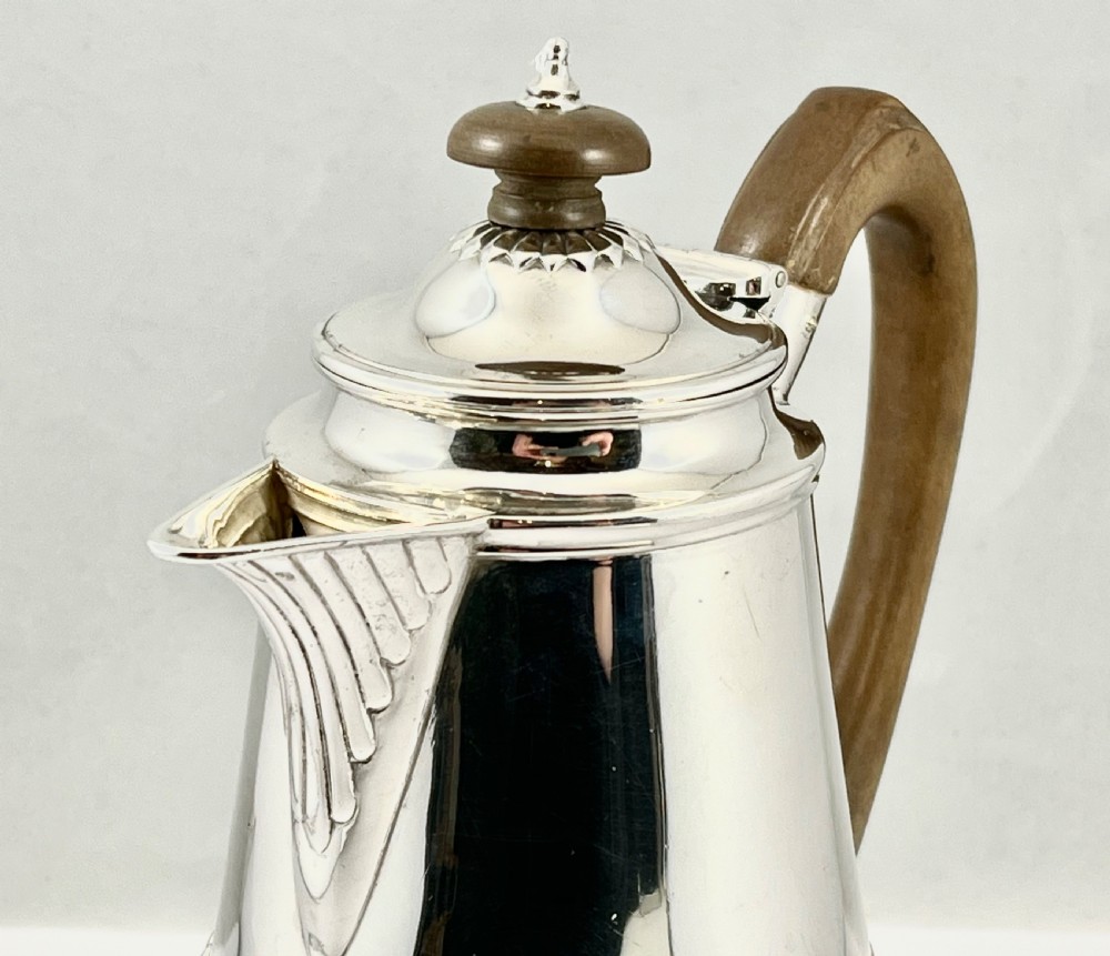 Victorian sterling silver hot water pot featuring a fluted lower body, hinged lid, and carved wooden handle. View VI