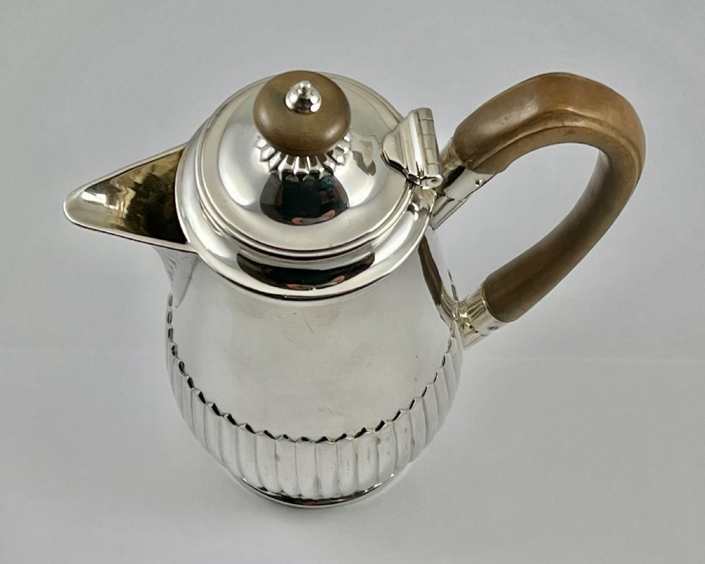 Victorian sterling silver hot water pot featuring a fluted lower body, hinged lid, and carved wooden handle. View VII