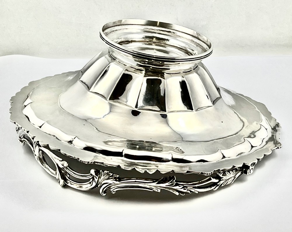 A round sterling silver bread basket featuring an overhead swing handle, floral engraving, a shell-detailed rim, and a fluted pedestal base. View V