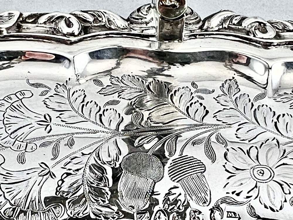 A round sterling silver bread basket featuring an overhead swing handle, floral engraving, a shell-detailed rim, and a fluted pedestal base. View VI