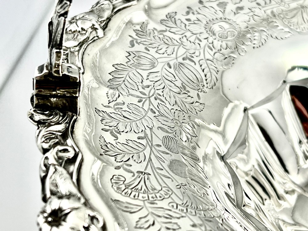 A round sterling silver bread basket featuring an overhead swing handle, floral engraving, a shell-detailed rim, and a fluted pedestal base. View VIII