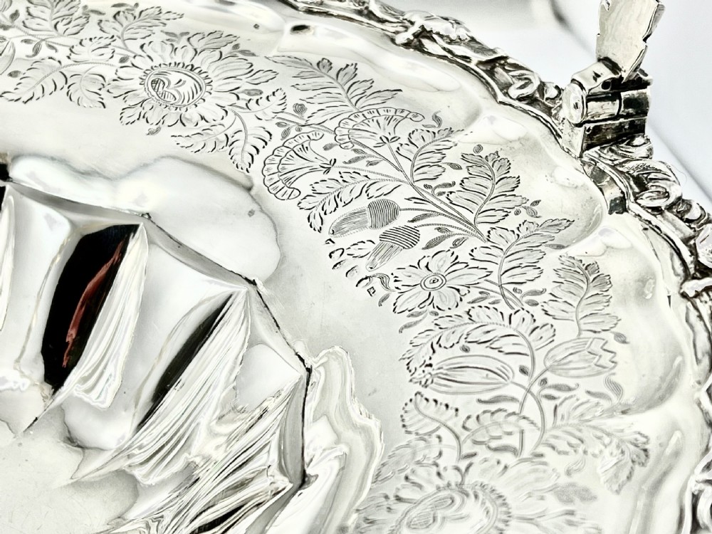 A round sterling silver bread basket featuring an overhead swing handle, floral engraving, a shell-detailed rim, and a fluted pedestal base. View IX