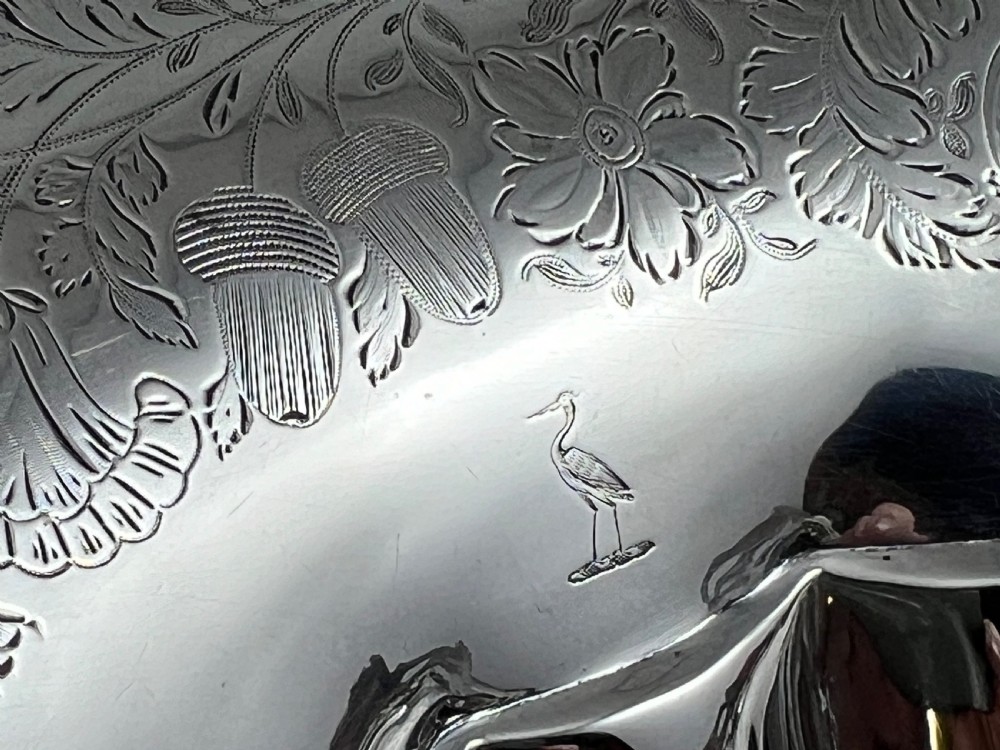 A round sterling silver bread basket featuring an overhead swing handle, floral engraving, a shell-detailed rim, and a fluted pedestal base. View XI