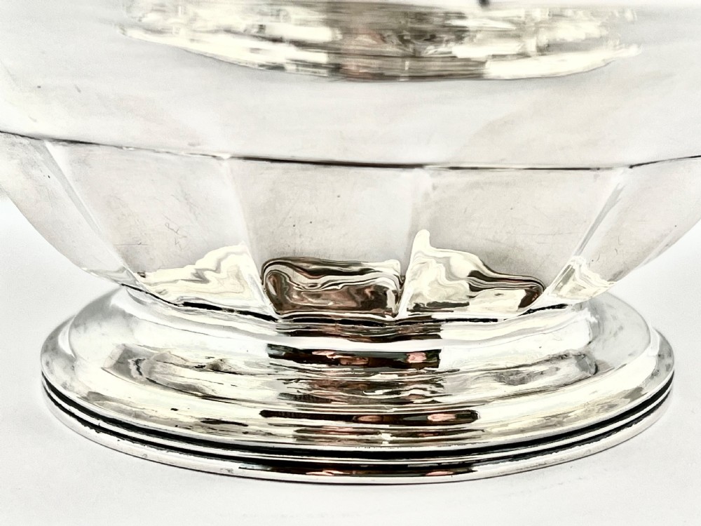 A round sterling silver bread basket featuring an overhead swing handle, floral engraving, a shell-detailed rim, and a fluted pedestal base. View XII