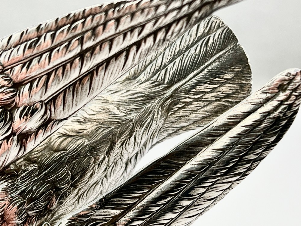 A chased Edwardian silver model of a wading bird with textured feather detail and webbed feet, shown in profile facing left. View X