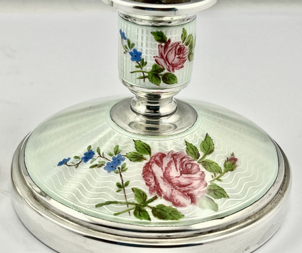 A pair of Elizabeth II sterling silver candlesticks featuring engine-turned white enamel bases and stems adorned with painted pink roses. View V