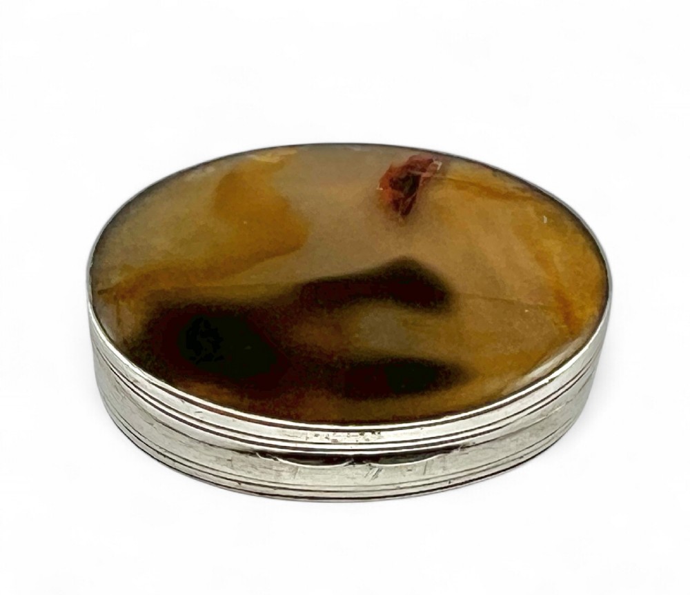 An oval George III sterling silver vinaigrette featuring reeded edge detailing and a polished brown agate inset in the lid.