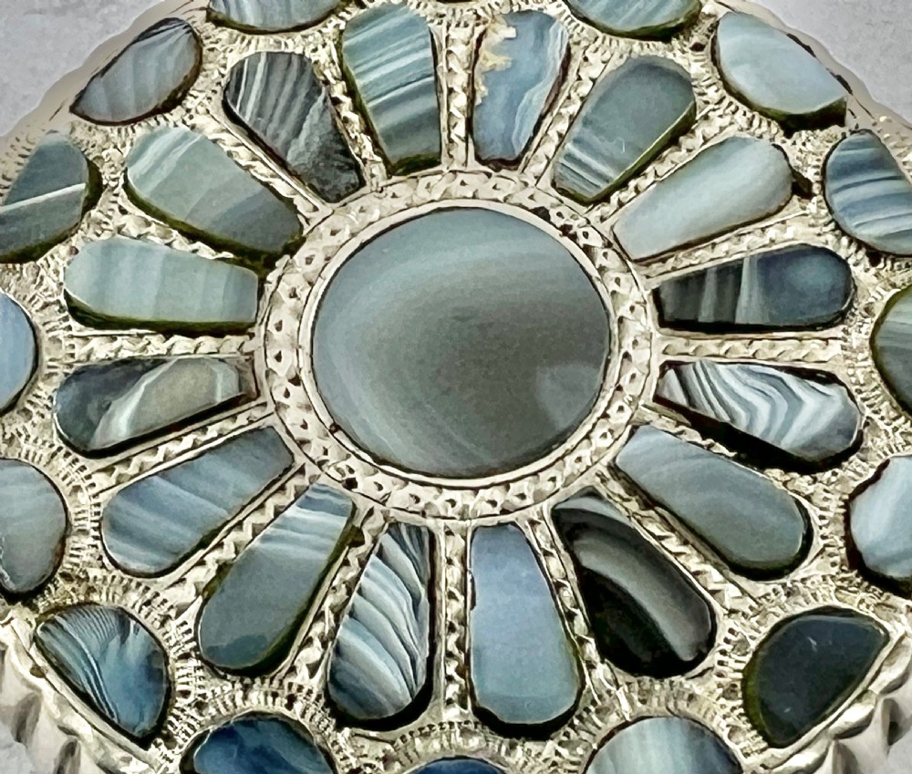 A circular Victorian silver brooch featuring a central round agate stone surrounded by radiating teardrop and crescent-shaped inlaid grey agates with an engraved border. View VII
