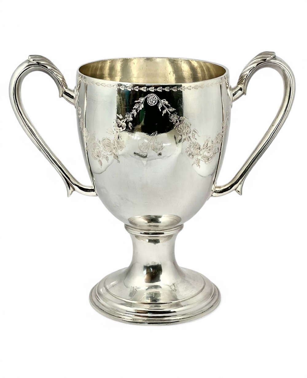 An 18th-century George III Scottish sterling silver two-handled cup featuring a stepped pedestal base, polished finish, and hand-engraved floral swags.