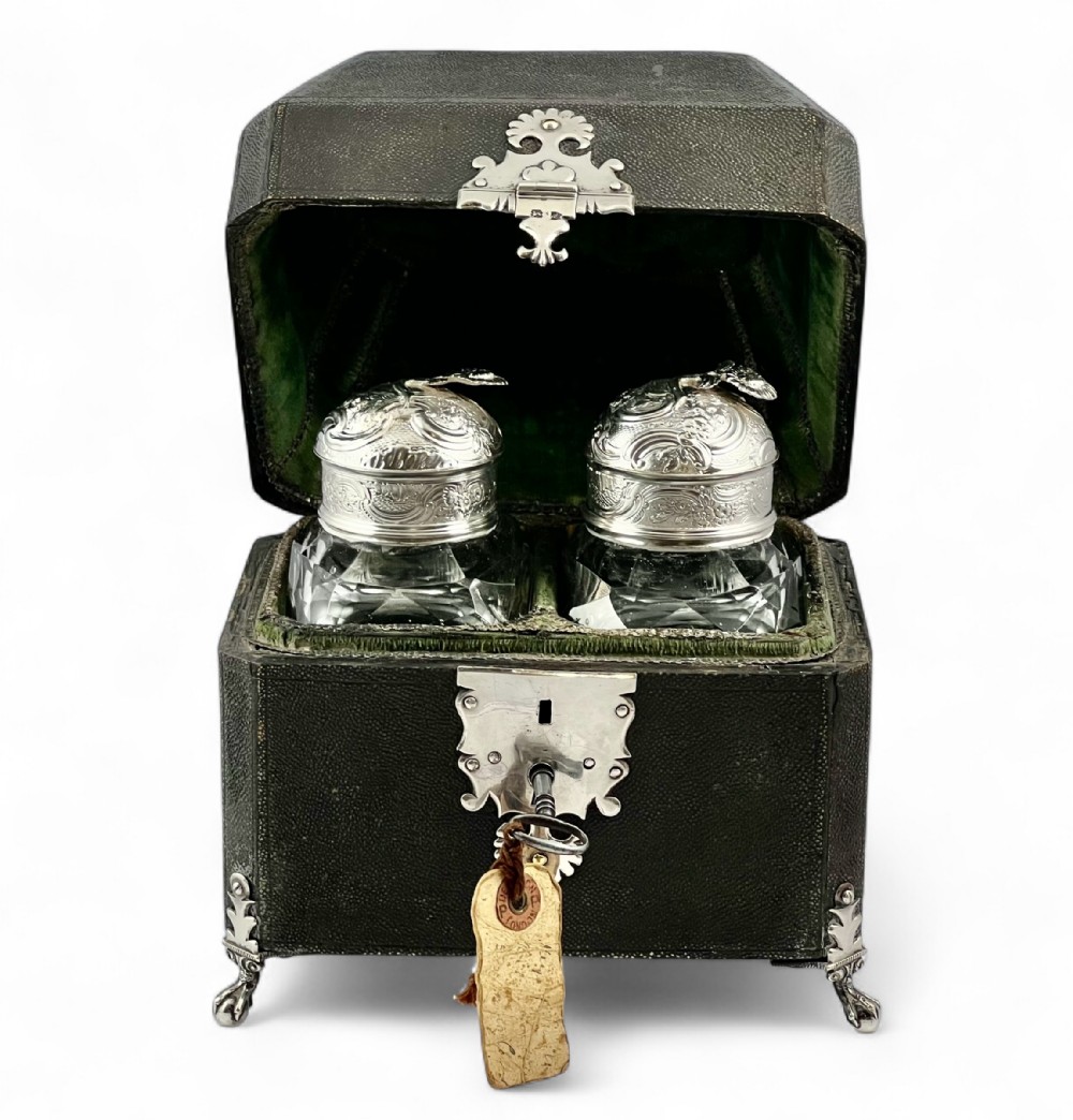 An open 18th-century dark green shagreen tea caddy featuring silver mounts, claw feet, and two cut-glass canisters with chased silver tops inside a green velvet-lined interior.