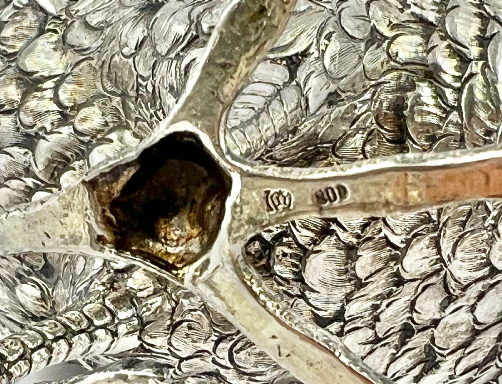 A detailed silver statue of a standing cockerel with finely chased feathering, a pronounced comb, and red stone eyes. View XI