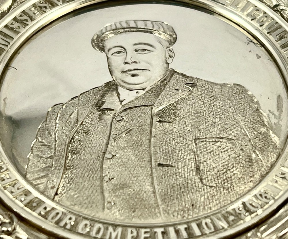 An Edwardian silver oval curling medal featuring crossed brooms at the top, a central engraved portrait of a man, and an inscribed silver border. View XI