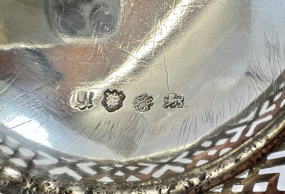 An 18th-century George II oval sterling silver basket featuring hand-pierced fretwork sides, an engraved central coat of arms, and an overhead swing handle. View V