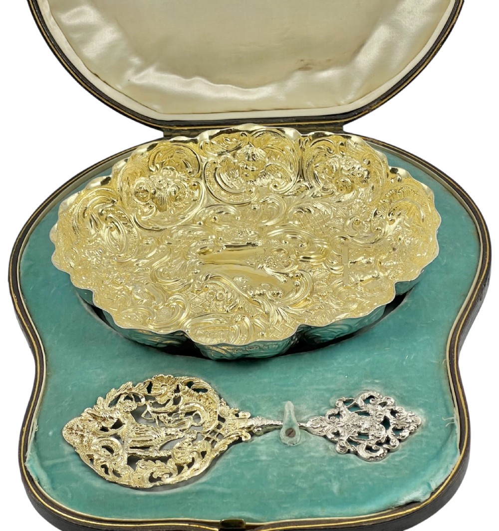 A Victorian silver-gilt scalloped dish with intricate repousse scrollwork and a matching pierced spoon, arranged inside a velvet-lined fitted presentation case.