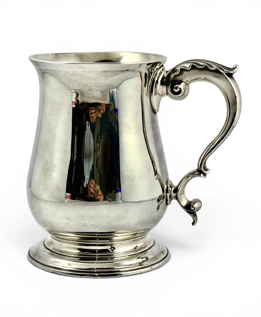A Georgian sterling silver pint tankard featuring a baluster-shaped body, double-scroll handle, and a moulded circular foot.