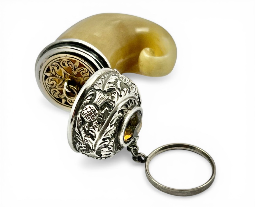 An antique Victorian Scottish vinaigrette made from a curved honey-coloured horn tip mounted with chased silver thistle patterns, a faceted yellow citrine gemstone, and an open hinged lid displaying an engraved gilt grille.