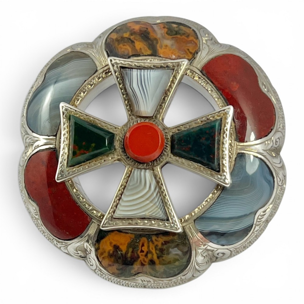 A circular Victorian Scottish silver brooch inlaid with polished agates, jasper, and bloodstone, featuring a central cross motif with engraved detailing.