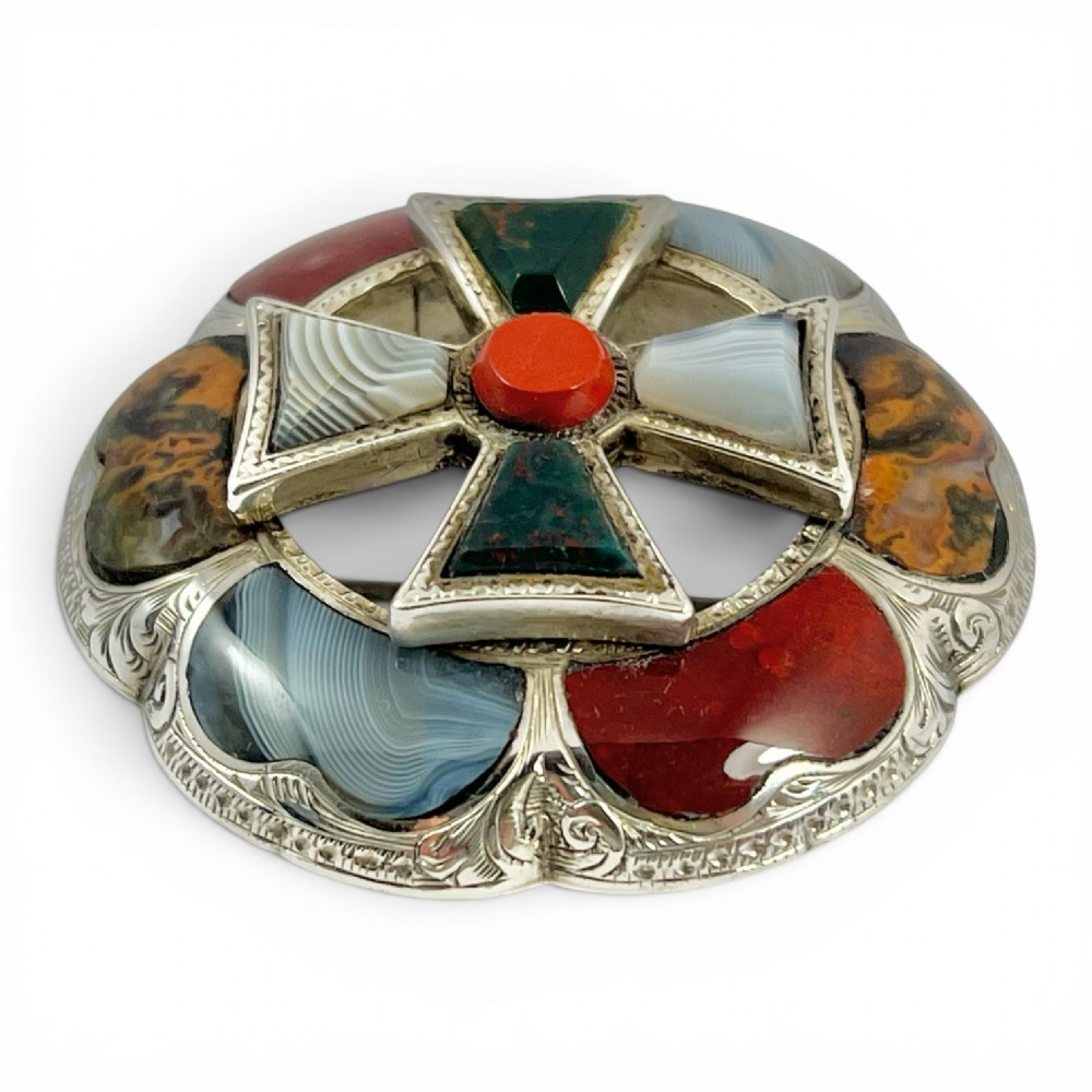 A circular Victorian Scottish silver brooch inlaid with polished agates, jasper, and bloodstone, featuring a central cross motif with engraved detailing. View II
