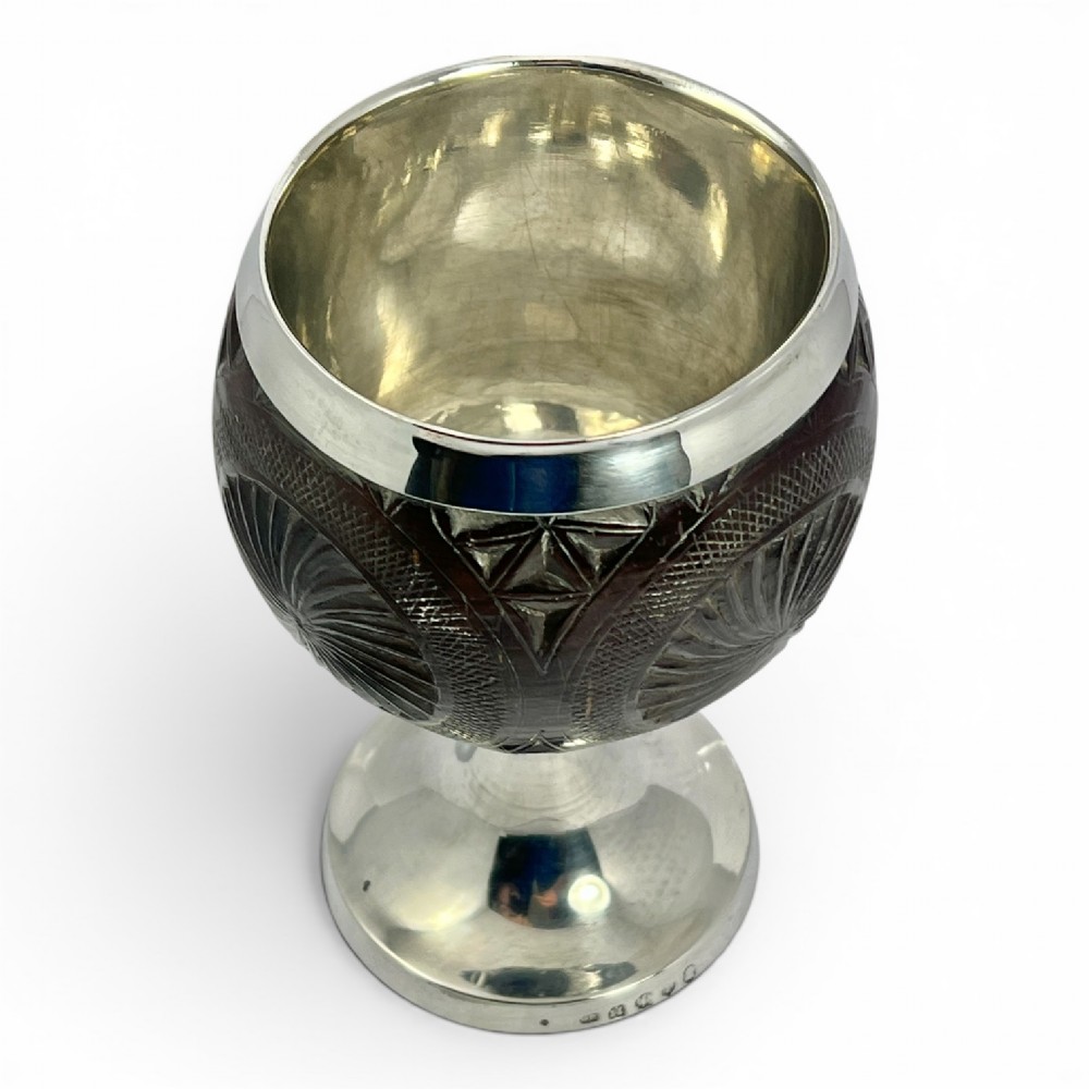 An eighteenth-century carved coconut shell goblet featuring intricate geometric starburst patterns, a silver rim, stem, and hallmarked circular base. View VII