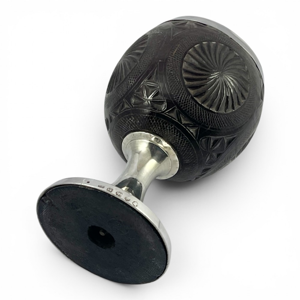 An eighteenth-century carved coconut shell goblet featuring intricate geometric starburst patterns, a silver rim, stem, and hallmarked circular base. View VIII