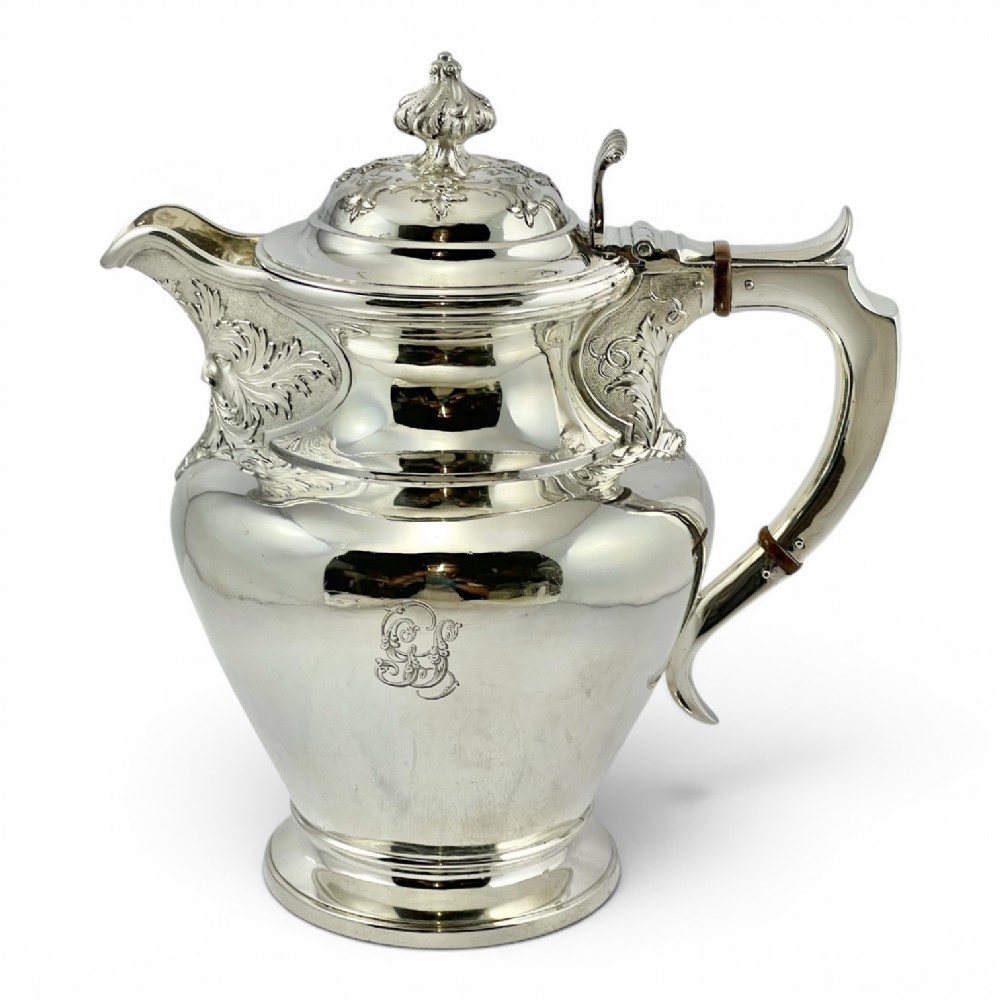 A William IV sterling silver water jug featuring a hinged domed lid, acanthus leaf relief carving, engraved monogram, and an angular insulated handle.