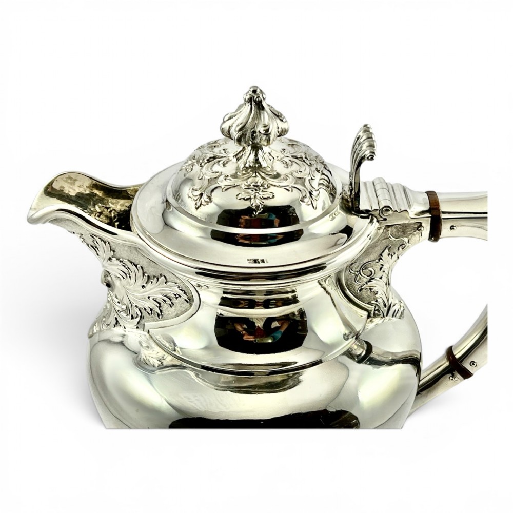 A William IV sterling silver water jug featuring a hinged domed lid, acanthus leaf relief carving, engraved monogram, and an angular insulated handle. View IV