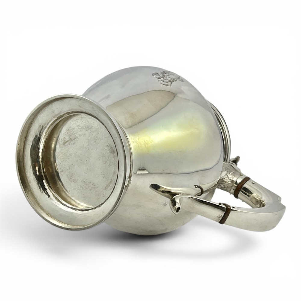 A William IV sterling silver water jug featuring a hinged domed lid, acanthus leaf relief carving, engraved monogram, and an angular insulated handle. View V