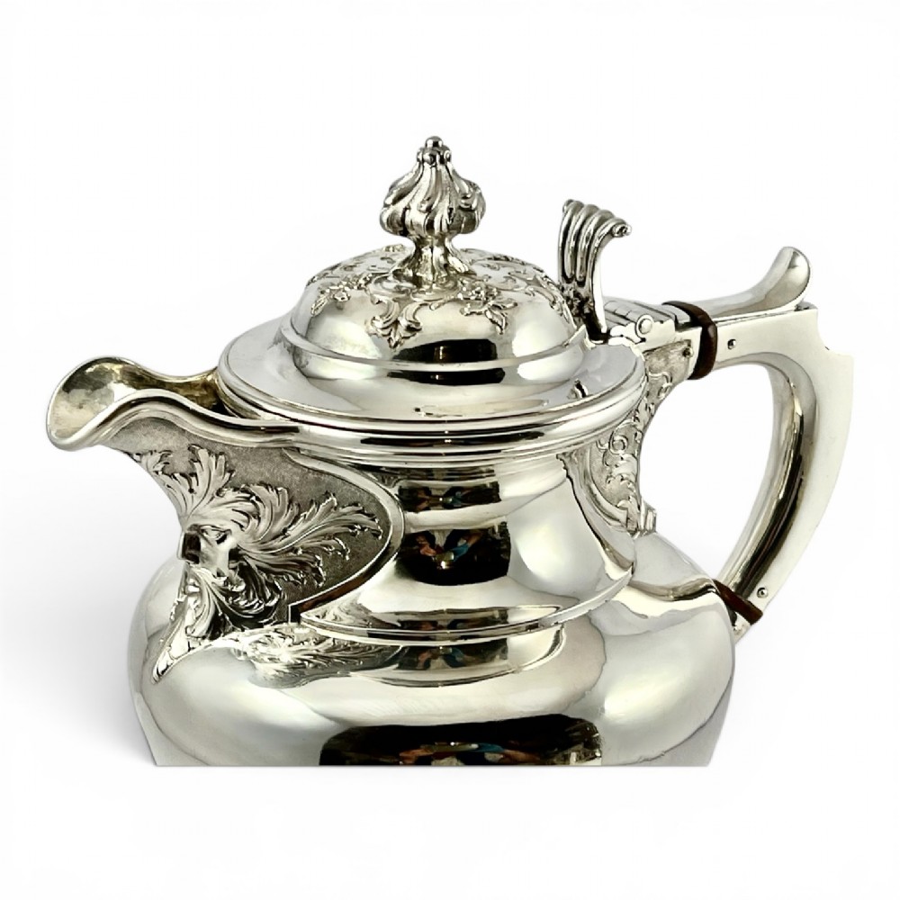 A William IV sterling silver water jug featuring a hinged domed lid, acanthus leaf relief carving, engraved monogram, and an angular insulated handle. View VI