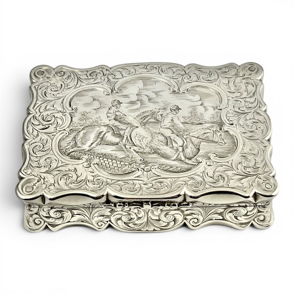 An early Victorian sterling silver table snuff box decorated with elaborate foliate engraving and a central equestrian scene of two jockeys riding horses.