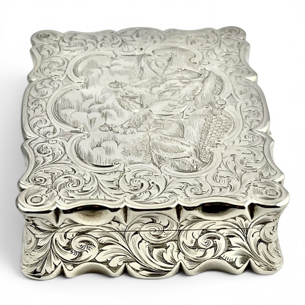 An early Victorian sterling silver table snuff box decorated with elaborate foliate engraving and a central equestrian scene of two jockeys riding horses. View II