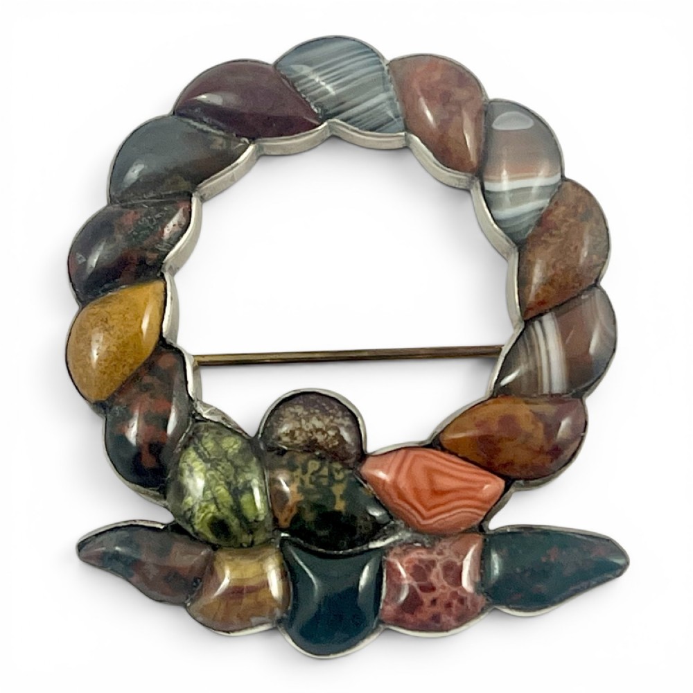 A circular Victorian Scottish silver brooch inlaid with polished multi-coloured agates and jaspers in a wreath pattern.