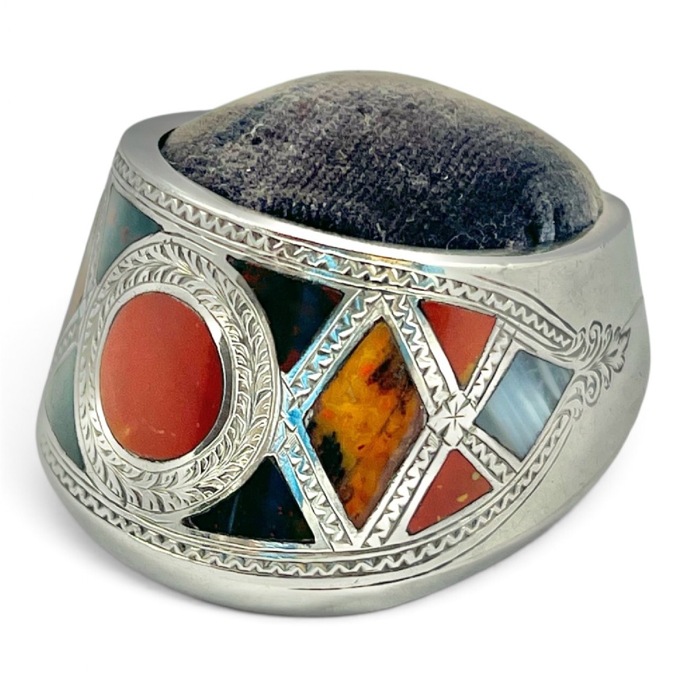 A Victorian silver pincushion shaped like a horse hoof, decorated with hand-engraved scrollwork and inlaid with geometric polished agates.