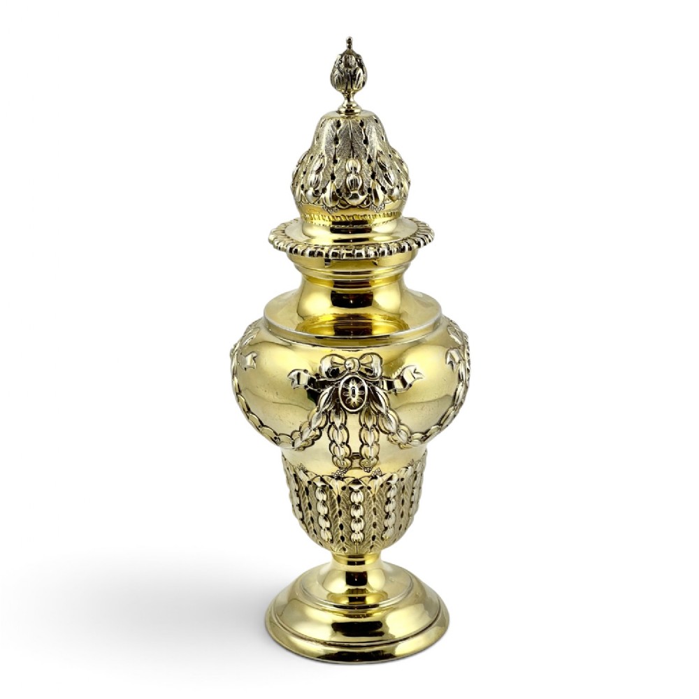An urn-shaped Edwardian silver-gilt sugar caster featuring ribbon bow and swag relief details with a pierced dome cover.