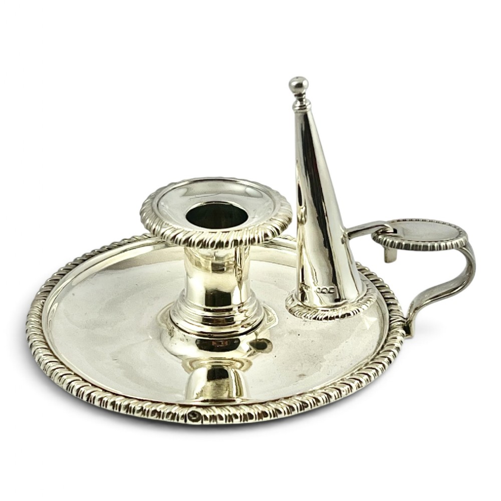 An 18th-century circular sterling silver chamberstick featuring a gadrooned rim, central sconce, scroll handle with thumbpiece, and a removable conical snuffer.