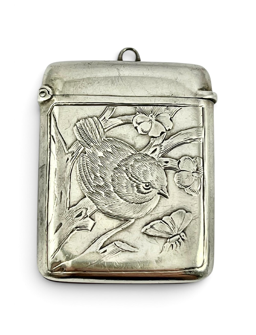 An Edwardian sterling silver vesta case decorated in relief with a bird perched on a branch, flowers, and a butterfly.
