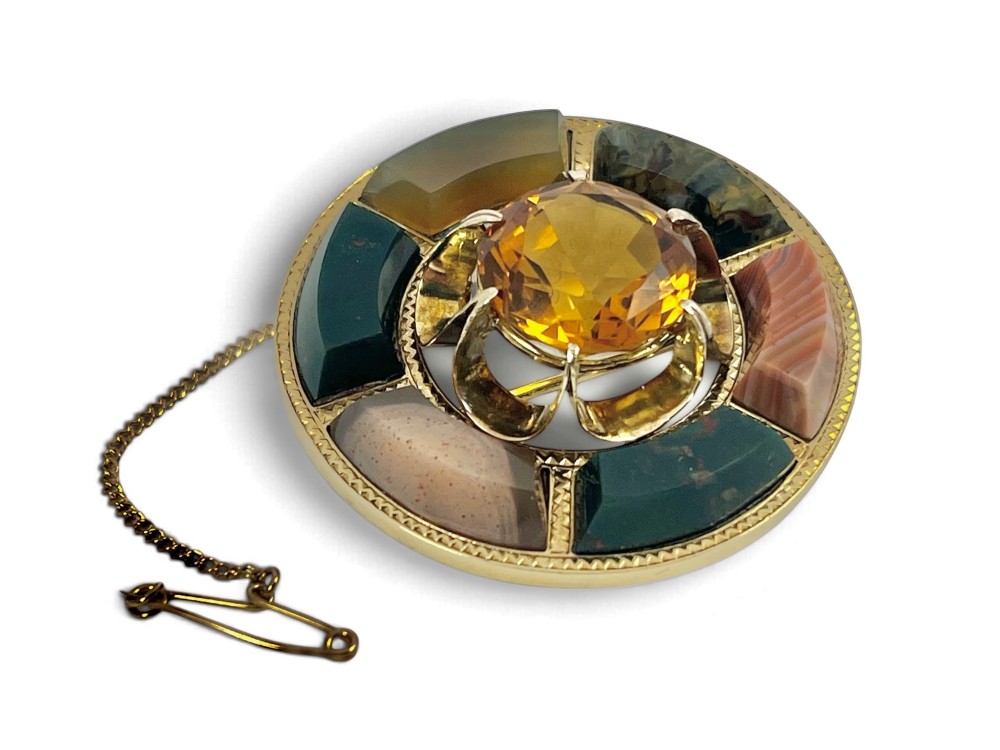 A circular Victorian 18ct gold brooch set with a central faceted yellow citrine gemstone surrounded by wedge-shaped inlaid agate and bloodstone panels, fitted with a safety chain. View VII