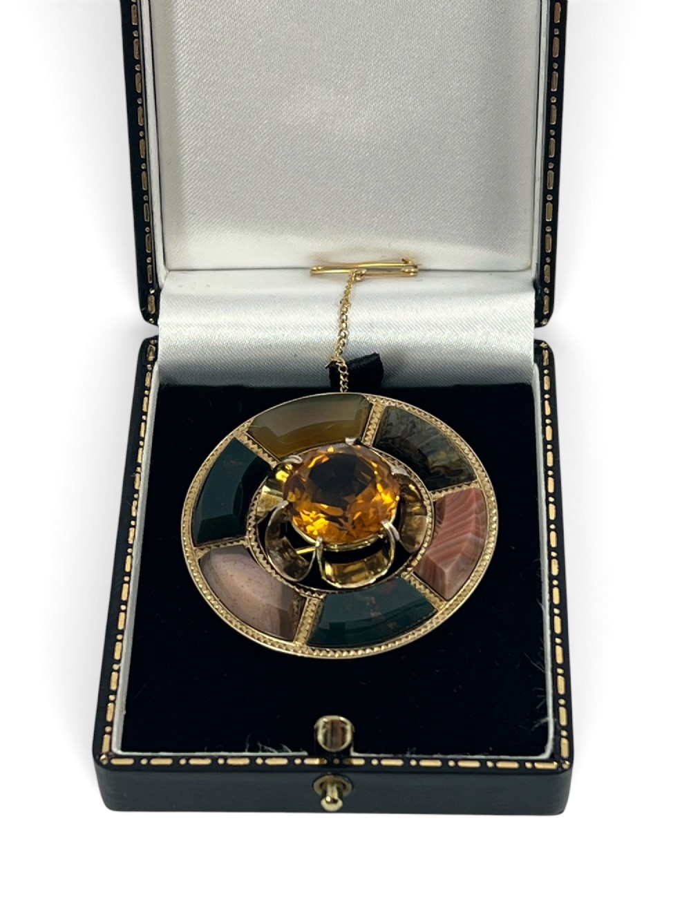 A circular Victorian 18ct gold brooch set with a central faceted yellow citrine gemstone surrounded by wedge-shaped inlaid agate and bloodstone panels, fitted with a safety chain. View VIII