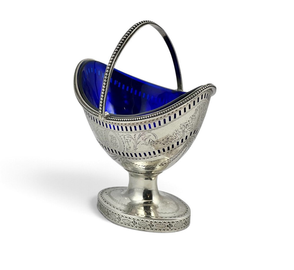 A George III sterling silver sugar basket featuring pierced geometric engraving, a beaded swing handle, a pedestal base, and a fitted cobalt blue glass liner. View III